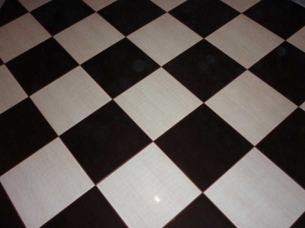 Ukończona podłoga z płytek w szachownicę, z ciemnymi i jasnymi kwadratami ułożonymi pod kątem, tworząc geometryczny wzór. Widok z góry.