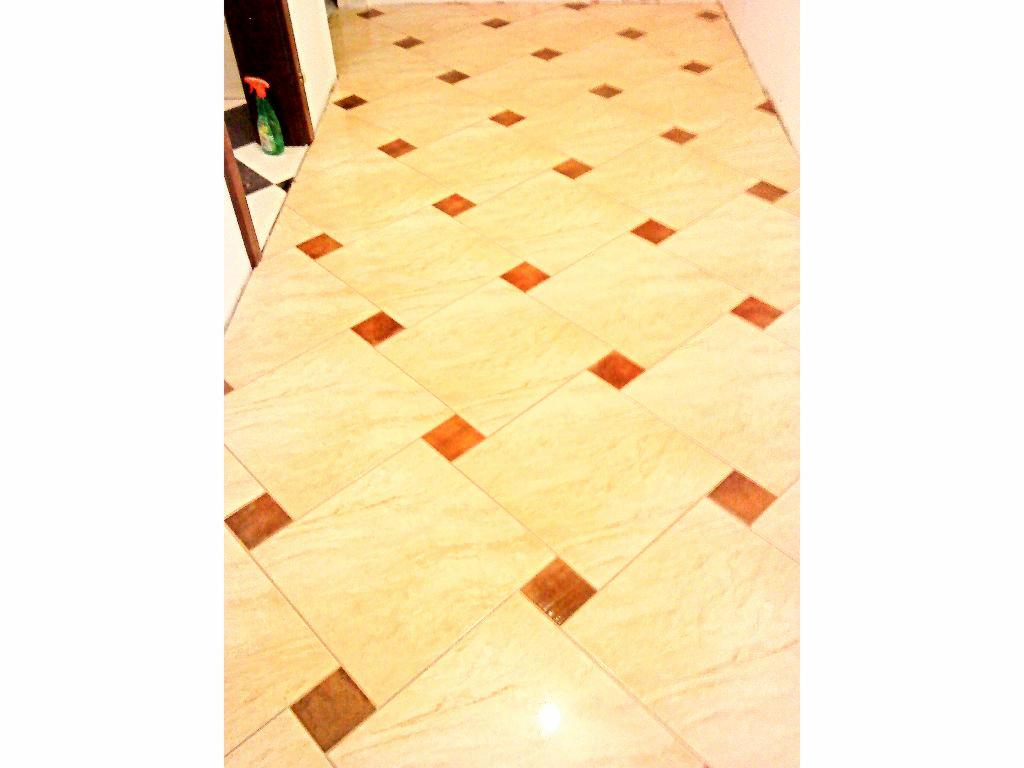 Jasne płytki podłogowe z brązowymi wstawkami ułożone w karo. W rogu butelka ze środkiem czyszczącym. Widok z góry.