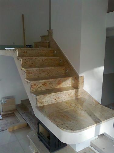Wykończone schody wewnętrzne z okładziną z kamienia naturalnego w odcieniach beżu i brązu. Widoczne elementy konstrukcyjne i przygotowanie do dalszych prac wykończeniowych.