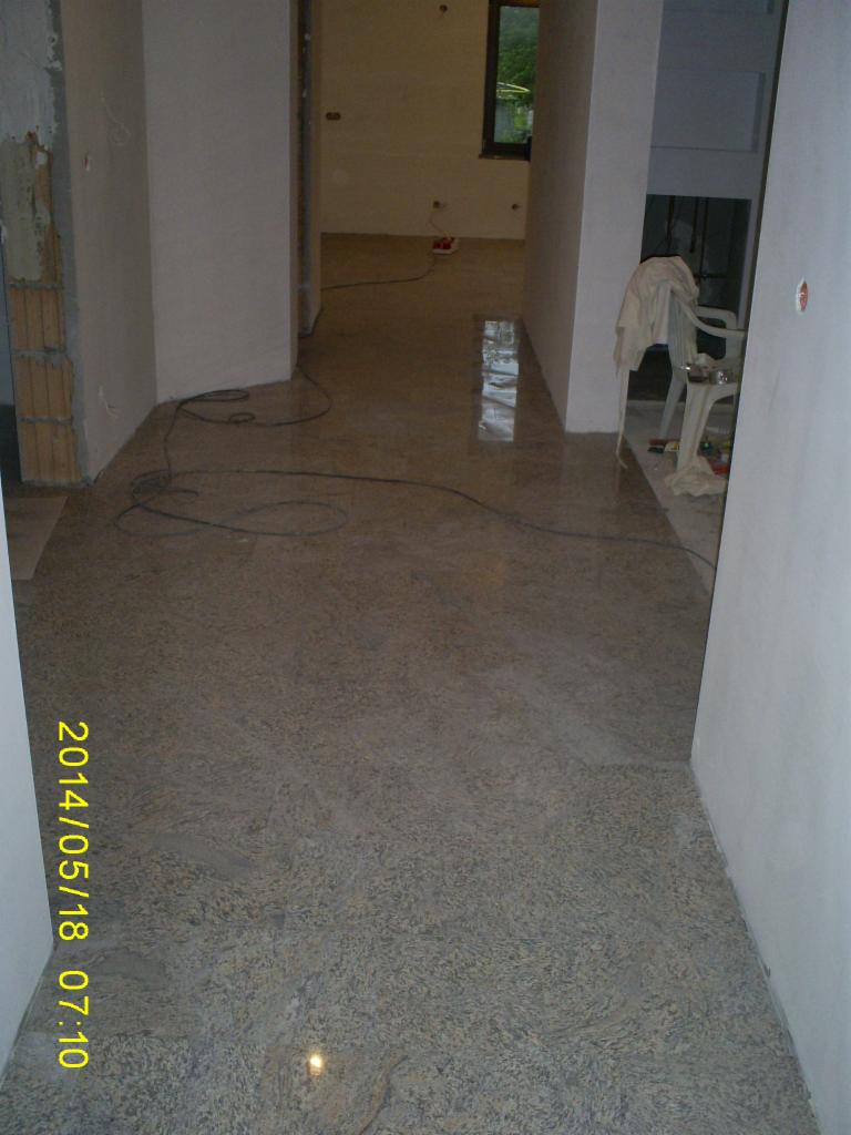 Wykończona podłoga z kamienia w jasnych odcieniach w nowym domu. Widoczne kable elektryczne i fragmenty ścian w trakcie prac wykończeniowych.