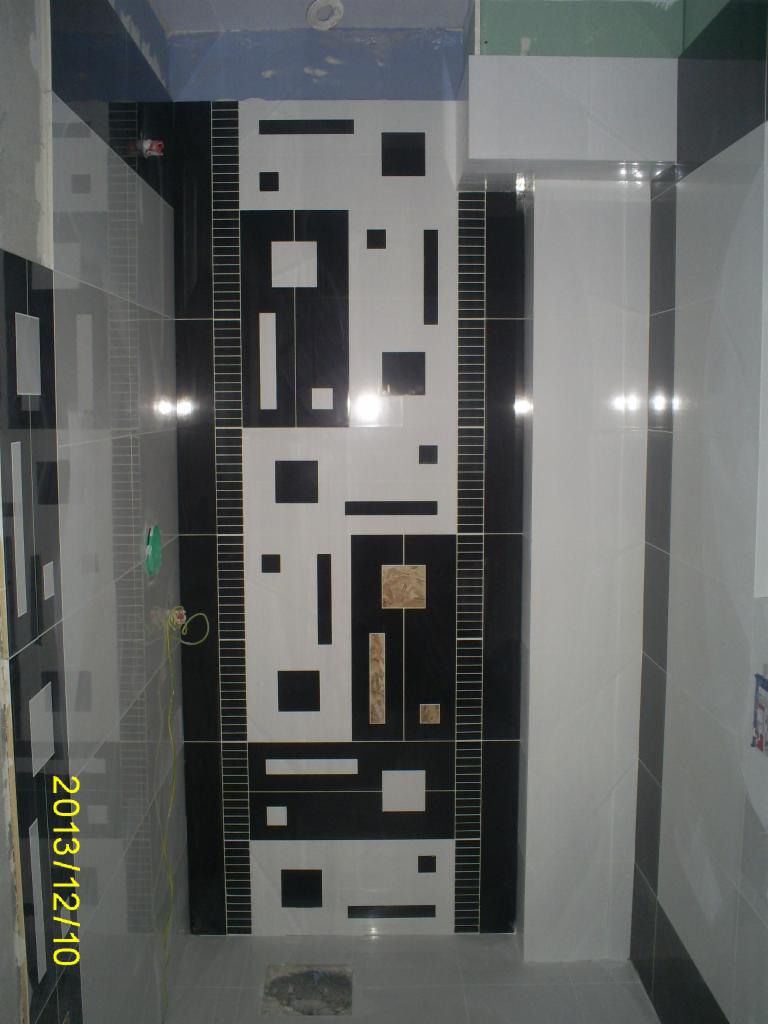 Wykończenie łazienki: ściana w czarno-białe geometryczne wzory z akcentami beżu, jasna podłoga, widok na fragment sufitu. Całość w nowoczesnym stylu.