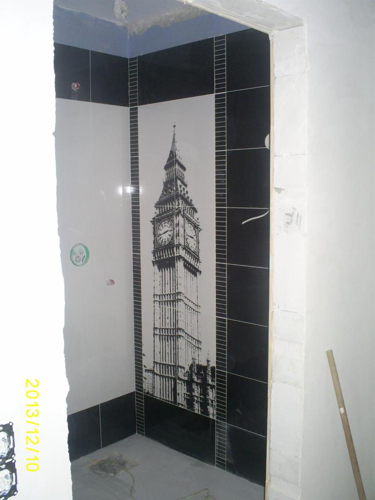 Wykończenie łazienki z czarno-białymi płytkami. Na ścianie dekoracyjna grafika Big Bena. Widoczne niedokończone prace wykończeniowe.