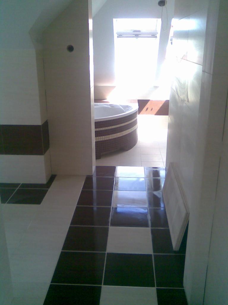 Nowoczesna łazienka z wanną w zabudowie mozaikowej. Podłoga w biało-czarną szachownicę. Jasne płytki ścienne i okno dachowe w tle.