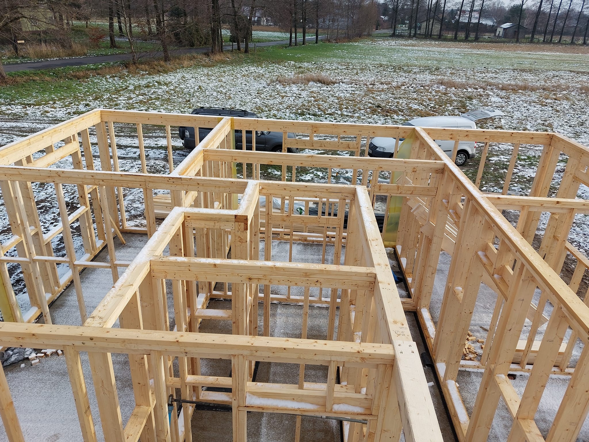 Wznoszenie drewnianej konstrukcji szkieletowej domu w zimowy dzień, widok z góry na jasne drewno i częściowo ośnieżony teren