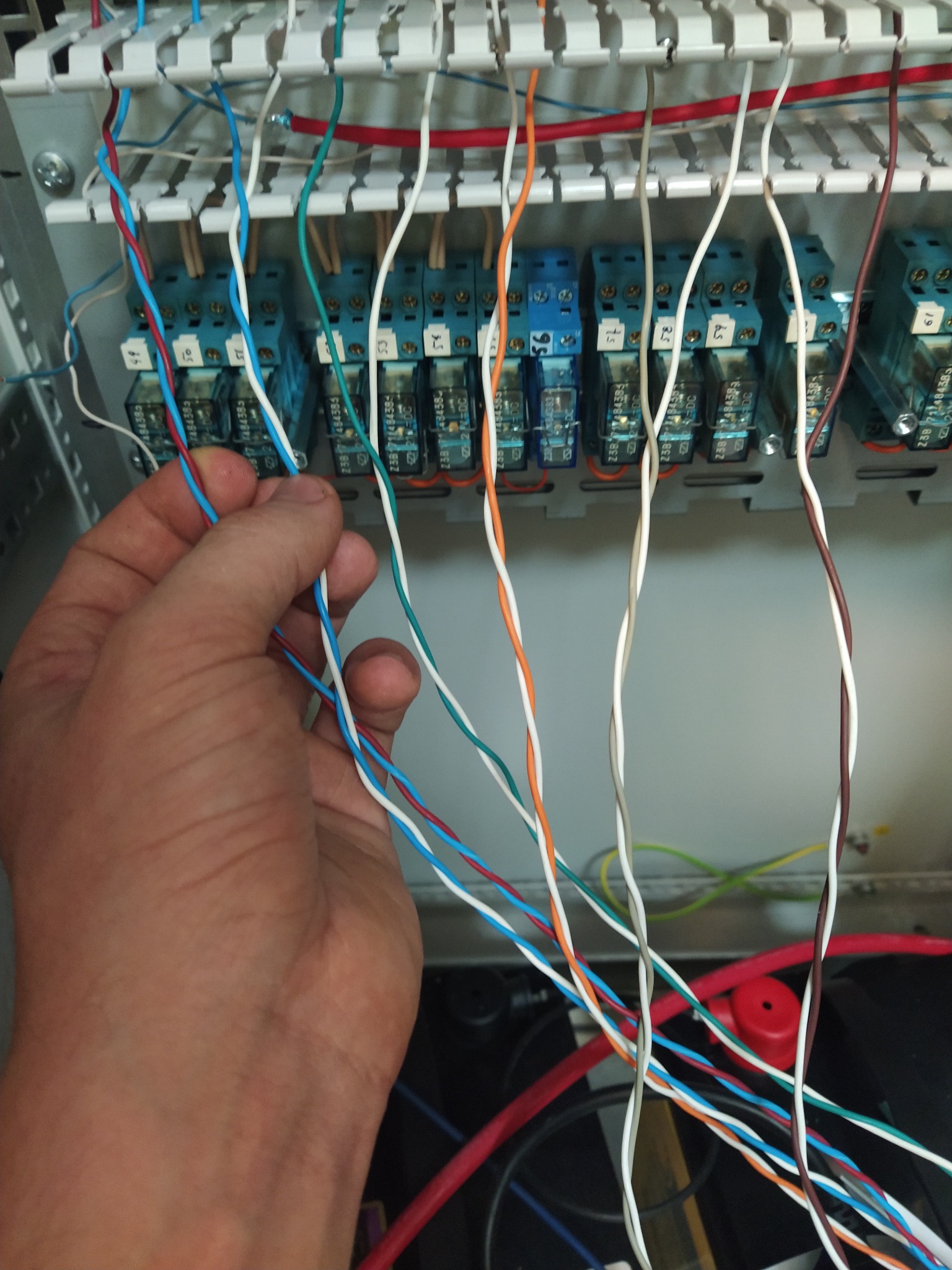 Ręka instalatora łączy kolorowe przewody w szafie sterowniczej z przekaźnikami, widoczne oznaczenia na przekaźnikach.