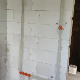 Ściana z betonu komórkowego z wyżłobieniami i puszkami instalacyjnymi w trakcie prac elektrycznych, widoczne kable w peszlu przy podłodze.