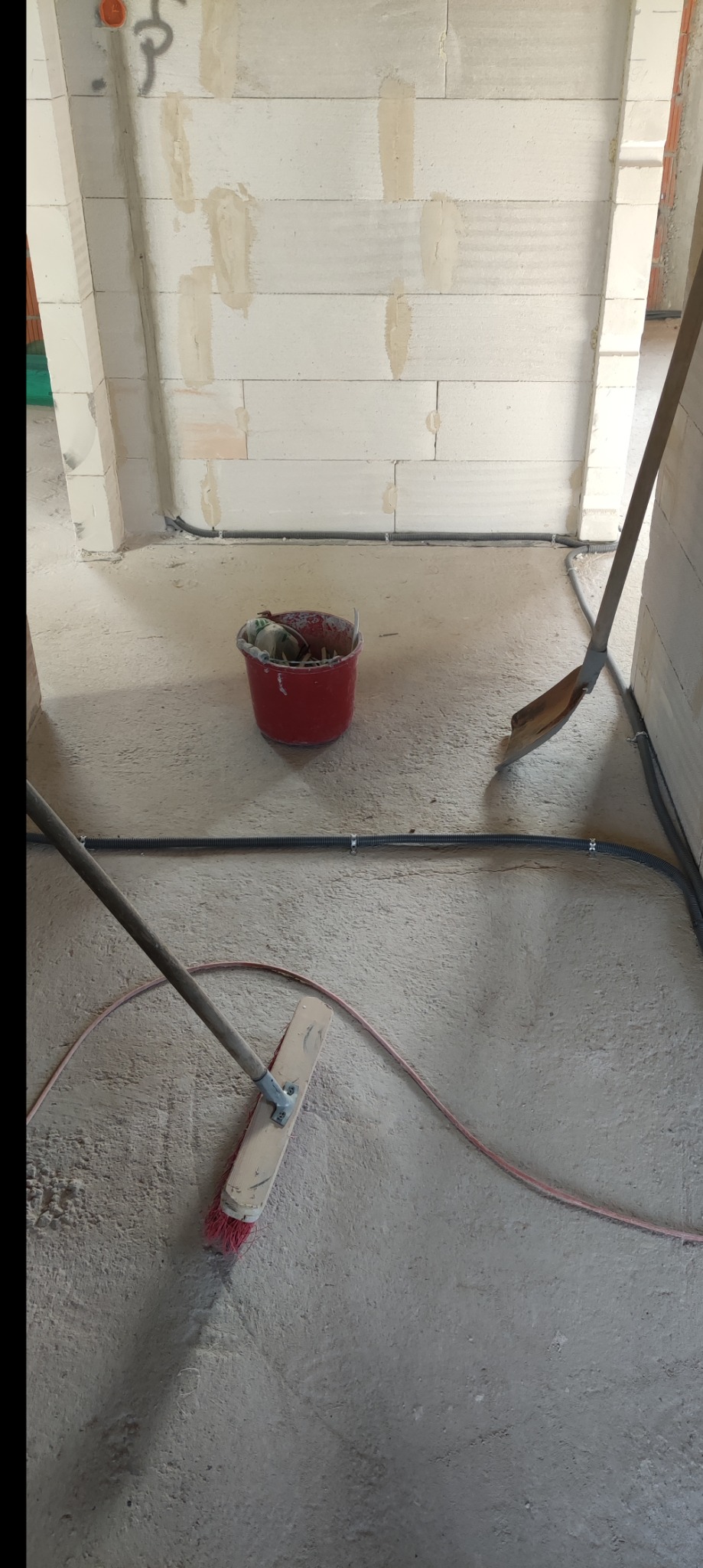 Przygotowanie do instalacji elektrycznej w nowym budynku: widoczne kable w peszlach ułożone wzdłuż ściany z betonu komórkowego, czerwone wiadro z narzędziami i miotła do sprzątania.