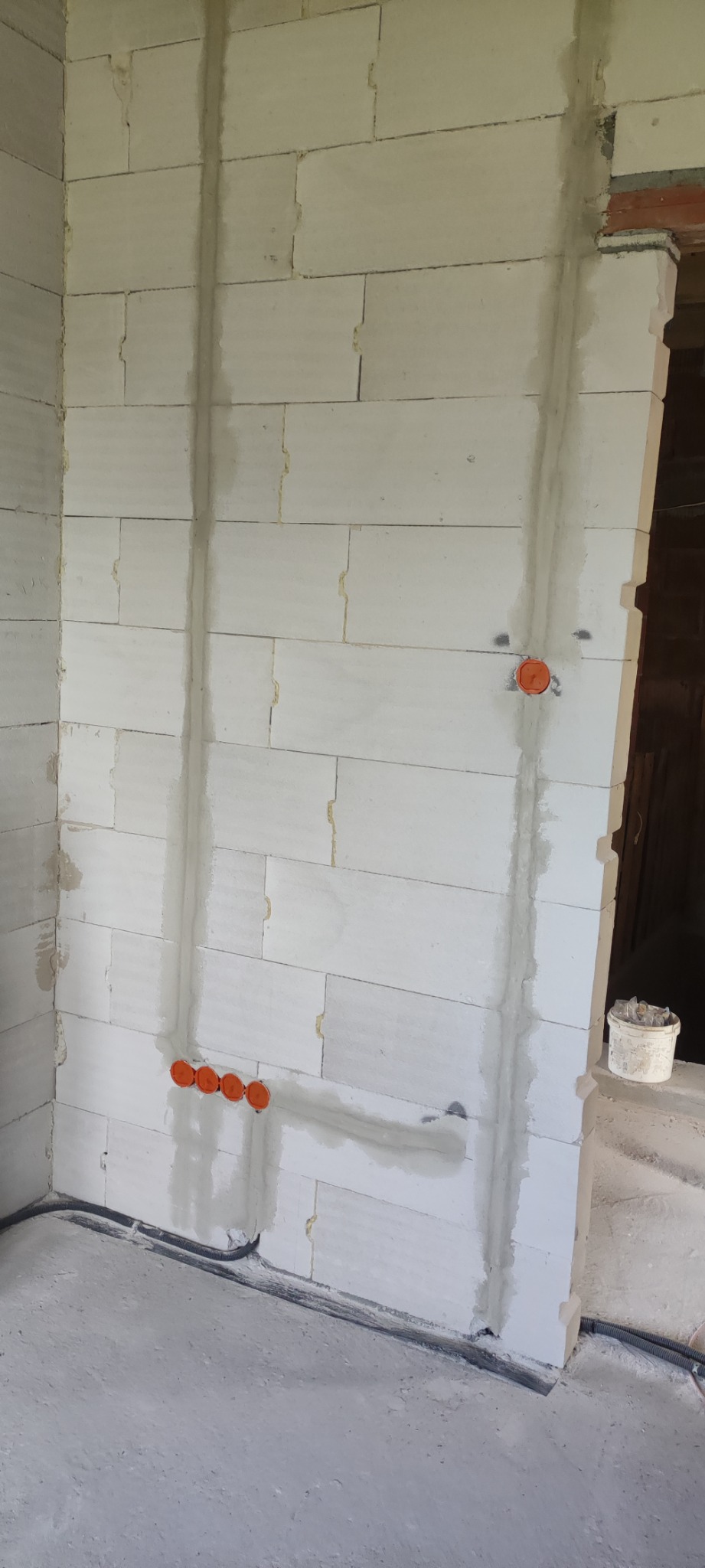 Ściana z betonu komórkowego z wyżłobieniami i puszkami instalacyjnymi w trakcie prac elektrycznych, widoczne kable w peszlu przy podłodze.
