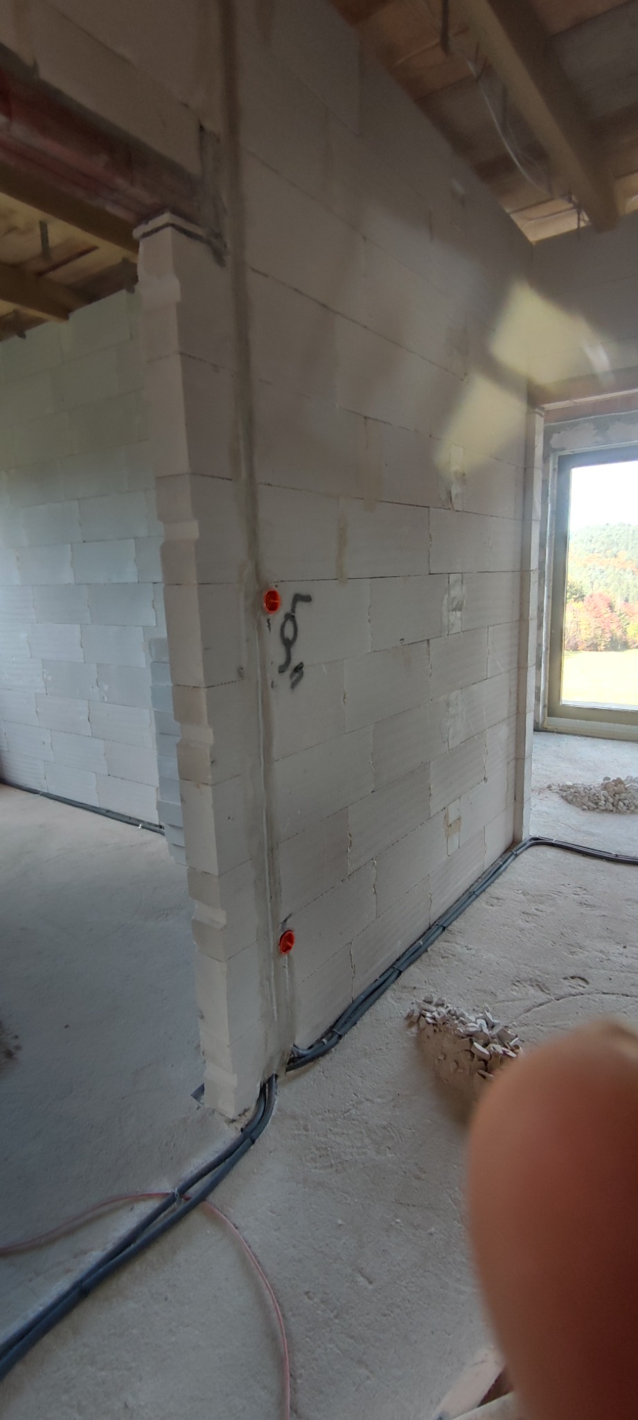 Surowy stan budynku z widocznymi przewodami elektrycznymi w peszlach, wystającymi ze ściany z betonu komórkowego, z zaznaczonymi punktami przyszłych gniazdek elektrycznych.