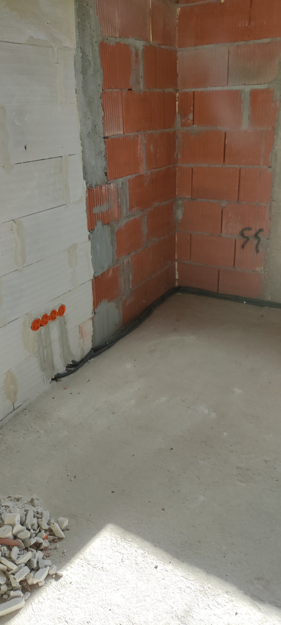 Surowy stan wnętrza z widocznymi przewodami elektrycznymi biegnącymi wzdłuż ściany z pustaków oraz czterema okrągłymi puszkami instalacyjnymi w ścianie z betonu komórkowego