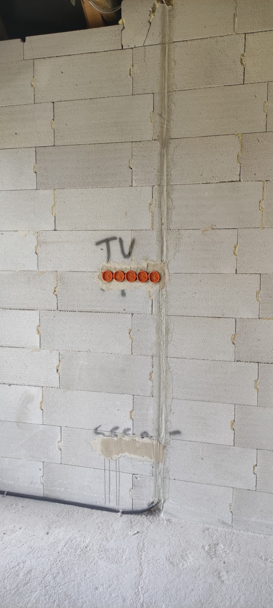 Ściana z betonu komórkowego w trakcie instalacji elektrycznej, widoczne pomarańczowe puszki pod gniazdka TV, bruzda zalana gipsem oraz peszel przy podłodze.