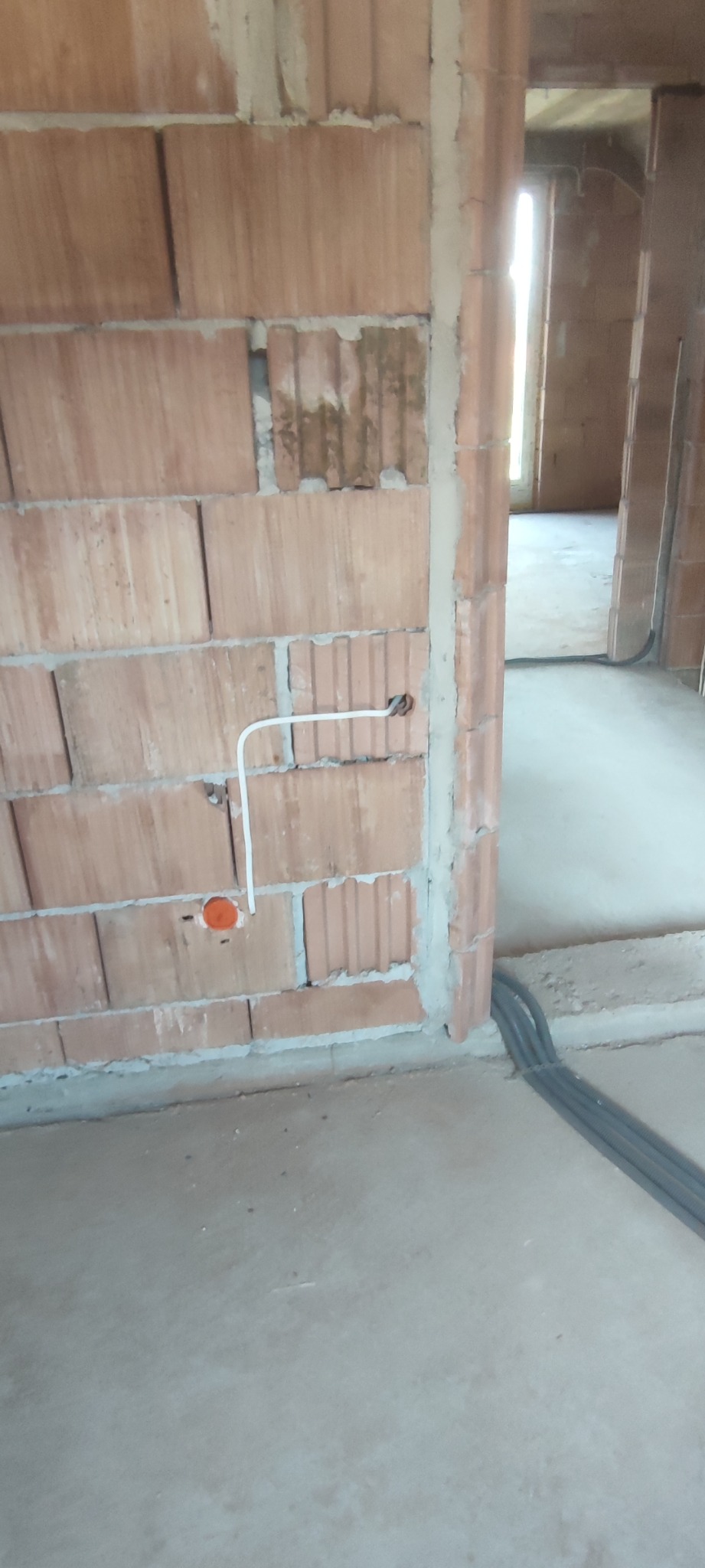 Wewnętrzna instalacja elektryczna w surowym budynku z cegły, widoczne przewody w peszlach i puszka instalacyjna.