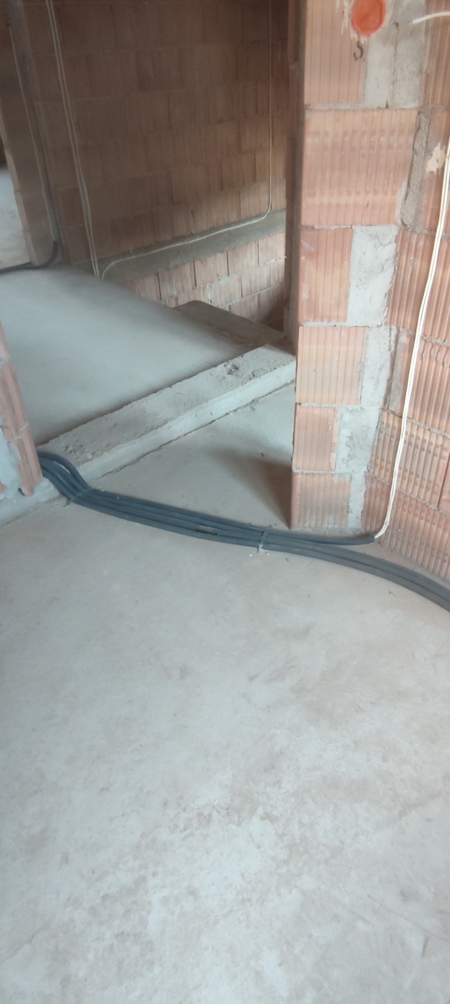 Wnętrze w trakcie budowy, widoczne kable elektryczne prowadzone wzdłuż ściany z cegły ceramicznej dziurawki i podłogi betonowej.