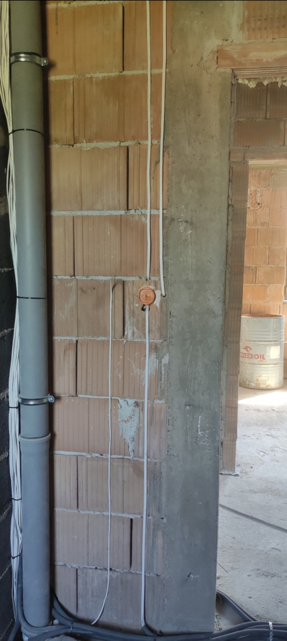 Surowa ściana z cegły z poprowadzonymi przewodami elektrycznymi, szara rura pionowa z kablami, widoczne puszki instalacyjne, stan surowy budynku.