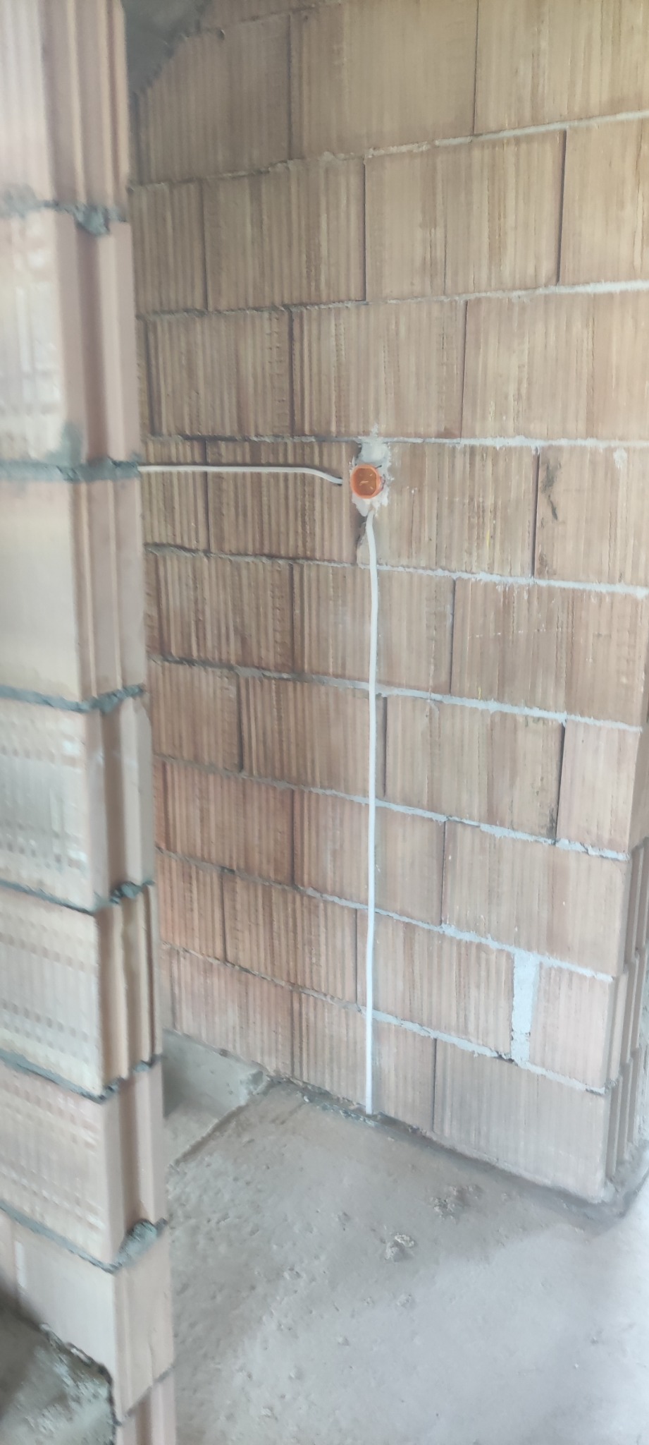 Wewnętrzna ściana z pustaków ceramicznych w trakcie budowy, z widoczną puszką elektryczną i poprowadzonym kablem w białej izolacji.