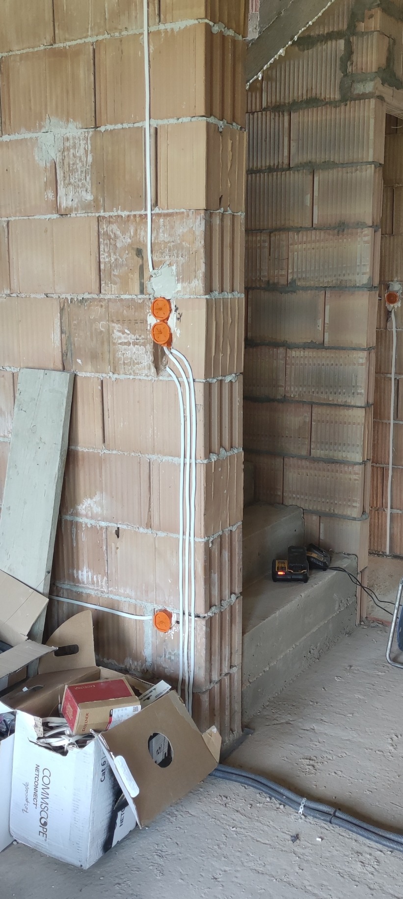 Wykonywanie instalacji elektrycznej w surowym budynku w Nowym Sączu: widoczne kable prowadzone po ścianach z cegły i pomarańczowe puszki elektryczne.