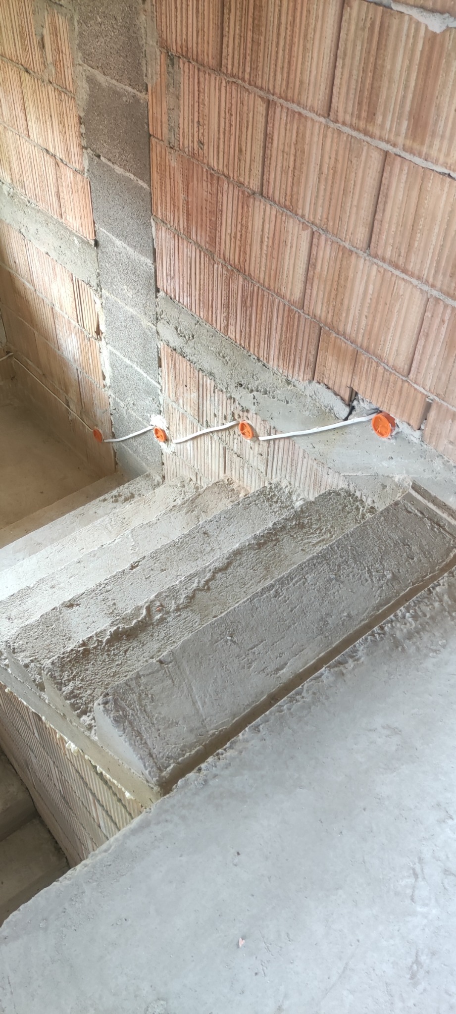 Surowe schody w trakcie budowy z widoczną instalacją elektryczną w peszlu i pomarańczowymi puszkami w ścianie z czerwonej cegły.