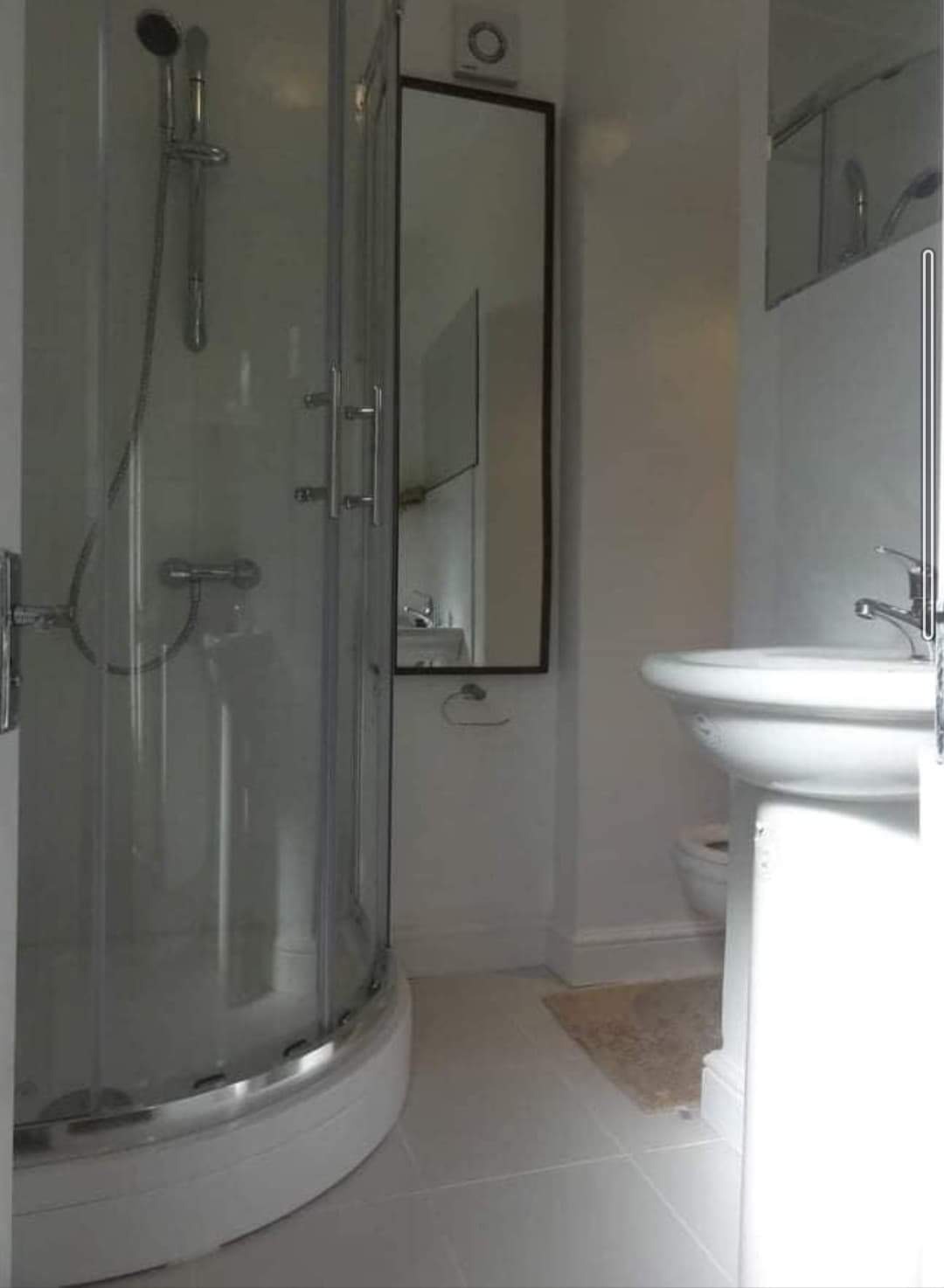 Nowoczesna, minimalistyczna łazienka z kabiną prysznicową narożną, umywalką na postumencie i lustrem w czarnej ramie.