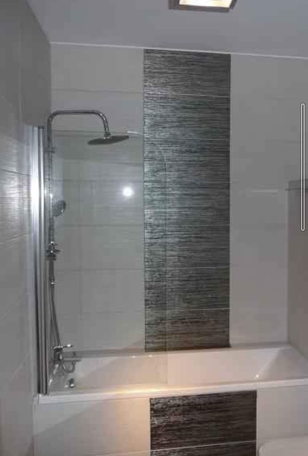 Wykończona łazienka z wanną, szklanym parawanem nawannowym i chromowaną armaturą prysznicową na tle płytek w odcieniach szarości z poziomym wzorem.