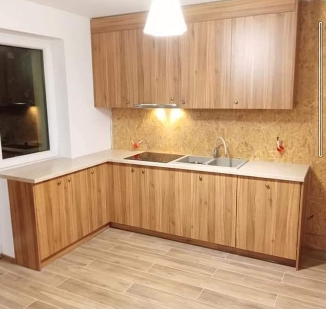 Nowoczesna kuchnia z drewnianymi szafkami, jasnym blatem i płytkami podłogowymi imitującymi drewno, widok z perspektywy podłogi, oświetlenie halogenowe pod szafkami górnymi.