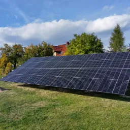 Panel słoneczny na trawniku przed domem jednorodzinnym w słoneczny dzień, widoczna sterta piasku.