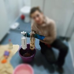 toczysto - Osoba w rękawicach trzymająca dwa elementy spłuczki toaletowej nad fioletowym wiadrem, w tle widoczna toaleta i podłoga w łazience.