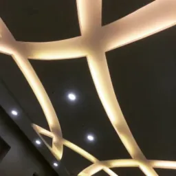 Dekoracyjny sufit podwieszany z podświetleniem LED tworzący geometryczny wzór krzyżujących się linii i punktowych lamp, widziany pod kątem.