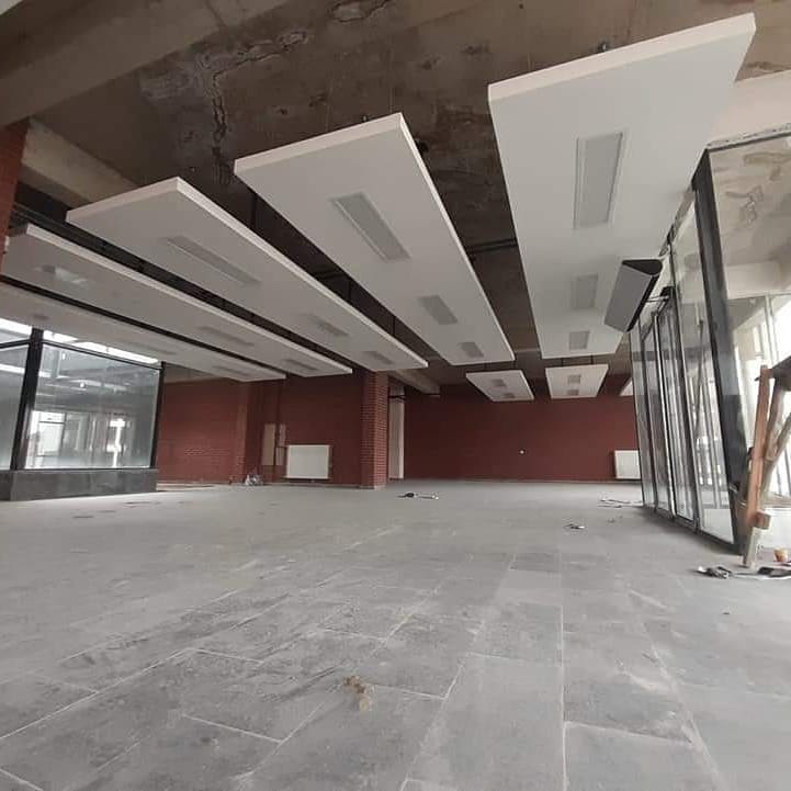 Wnętrze biura w trakcie wykańczania z zamontowanymi podwieszanymi panelami sufitowymi z oświetleniem, widoczne ceglane filary i szklane ściany.