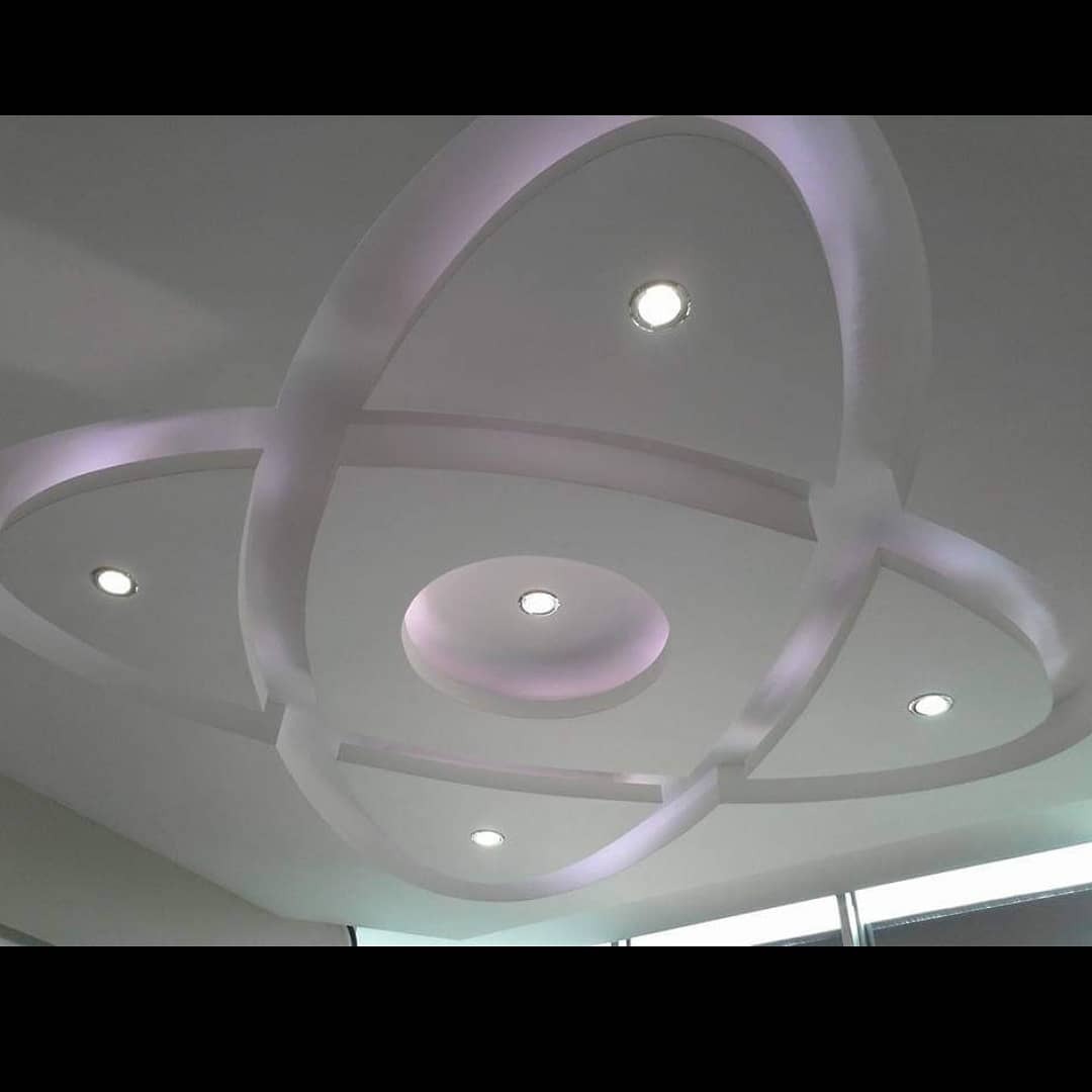 Dekoracyjny sufit podwieszany z oświetleniem punktowym, krzyżujące się łuki tworzące geometryczny wzór, widoczne okno w tle.