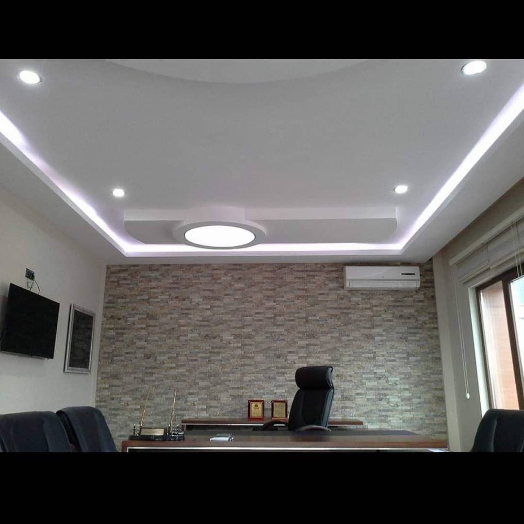 Biuro z podwieszanym sufitem z oświetleniem LED, kamienną ścianą i klimatyzacją, widok na ciemne biurko i krzesła.