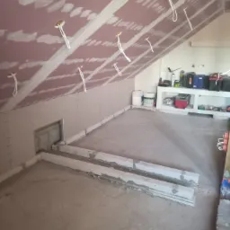 Poddasze w trakcie ocieplania z widoczną konstrukcją z płyty karton gips z wyprowadzonymi przewodami elektrycznymi i dwiema długimi belkami na podłodze.