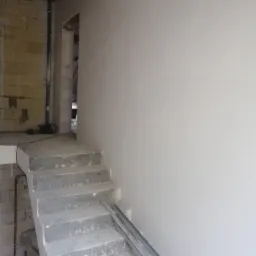 Surowe schody betonowe w trakcie prac wykończeniowych, z widoczną gładzią na ścianie i profilem aluminiowym na schodach, w tle ściana z pustaków.