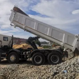 Wyładowywanie kruszywa z białej wywrotki na placu budowy, w tle widoczna ż&oacute;łta ładowarka kołowa Volvo.