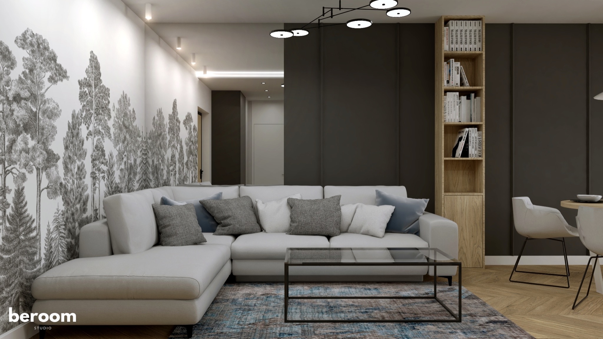 Jasny narożnik z szarymi poduszkami na tle ściany z motywem leśnym, szara ściana z regałem na książki, szklany stolik kawowy i parkiet na podłodze.