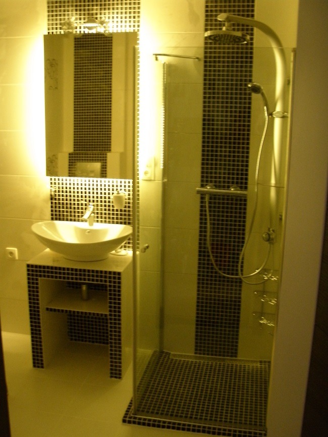 Nowoczesna łazienka z kabiną prysznicową i umywalką nablatową na szafce wykończonej mozaiką, zrealizowana w Lubinie. Oświetlenie LED w lustrze i pod prysznicem.