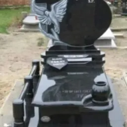 Czarny, polerowany pomnik z granitu z motywem serca, krzyża i gołębia, z inskrypcjami na tabliczkach i wazonem na kwiaty.