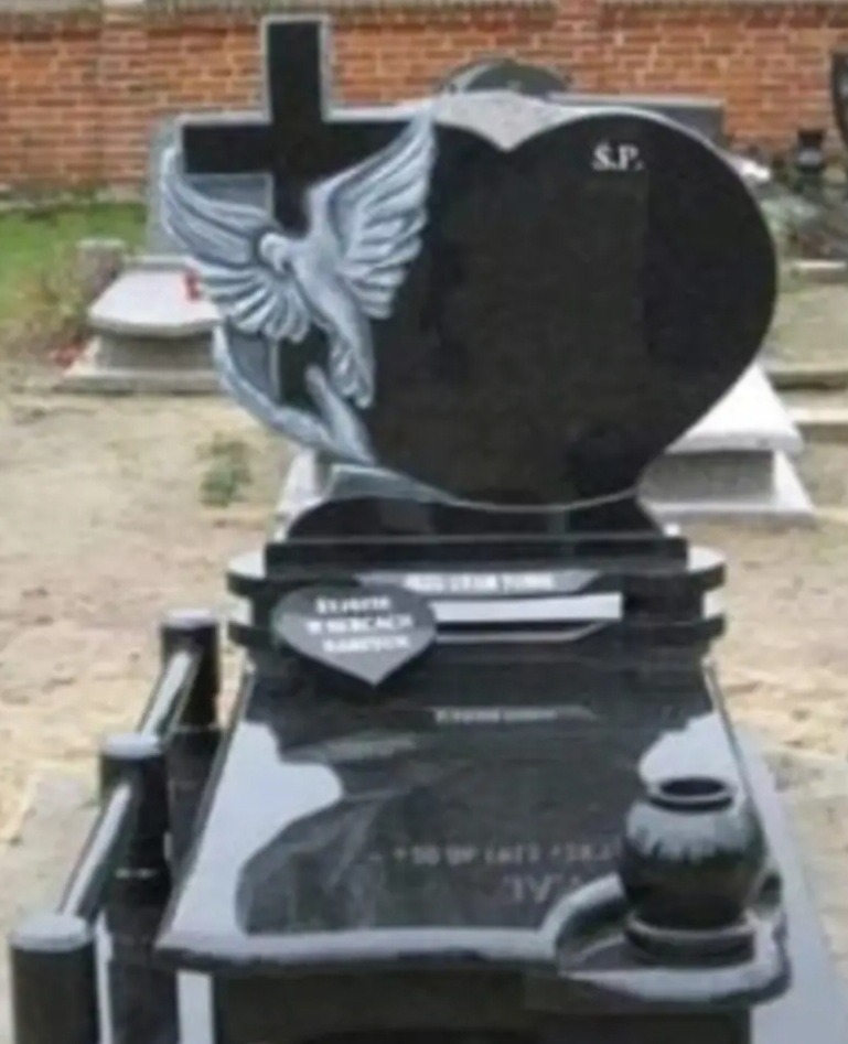 Czarny nagrobek z krzyżem, motywem gołębicy i sercem, na cmentarzu, z napisem 'S.P.'