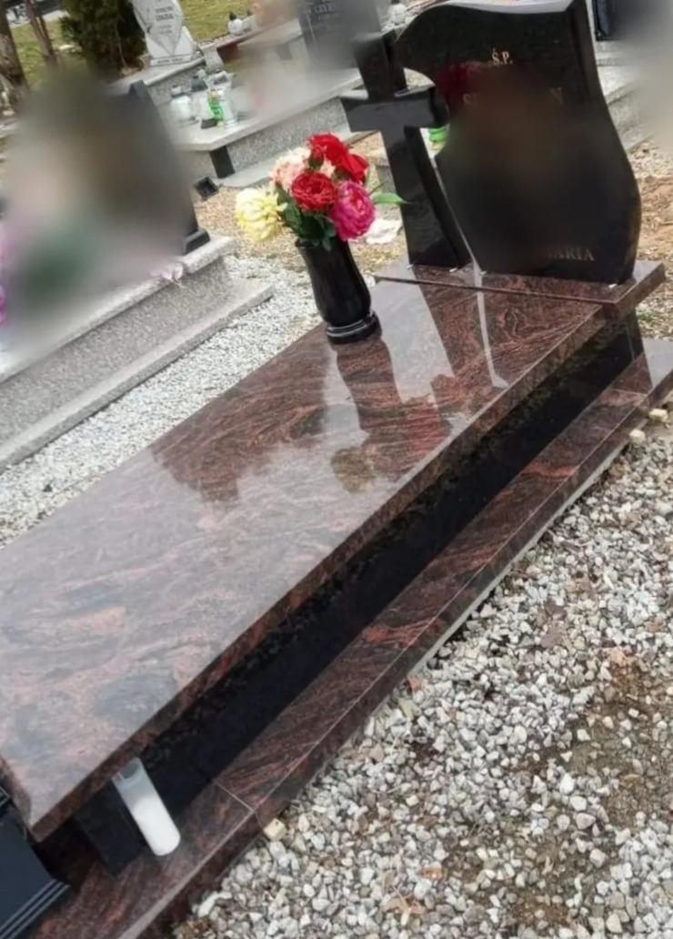 Polerowany, dwupoziomowy pomnik z brązowego granitu z czarnym krzyżem i wazonem z czerwono-różowymi różami, otoczony żwirem.