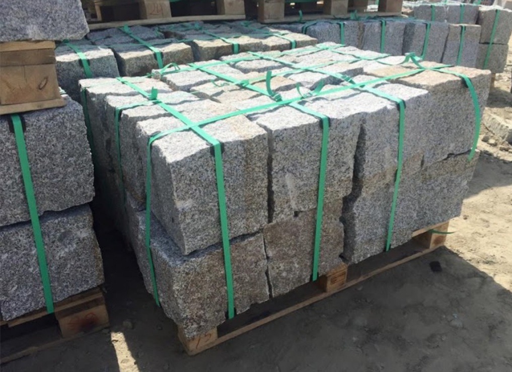 Kostka granitowa w blokach, zabezpieczona zieloną taśmą na drewnianej palecie, gotowa do transportu.