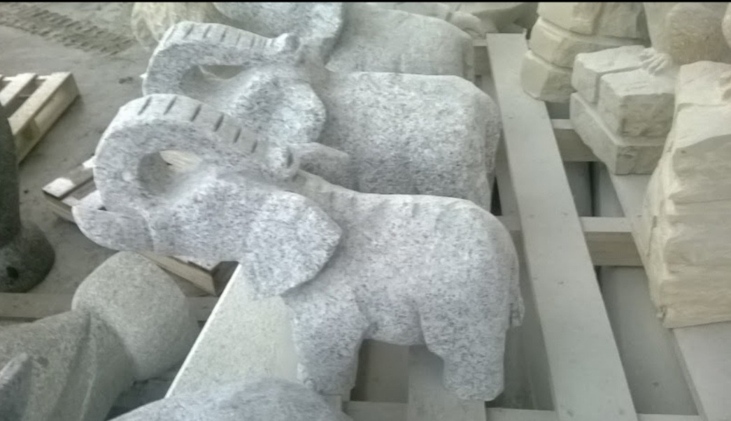 Szare, granitowe figurki słoni ustawione na paletach, prawdopodobnie przygotowane do transportu.