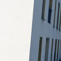 Fragment białej elewacji budynku z pionowymi wnękami i oknami, widzianej pod kątem, z wyraźnym cieniem na gładkiej powierzchni.