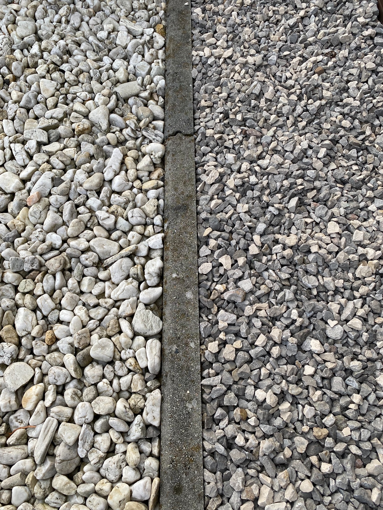 Podział na dwie strefy: białe otoczaki po lewej stronie i szare kamienie łamane po prawej, oddzielone betonową obwódką.