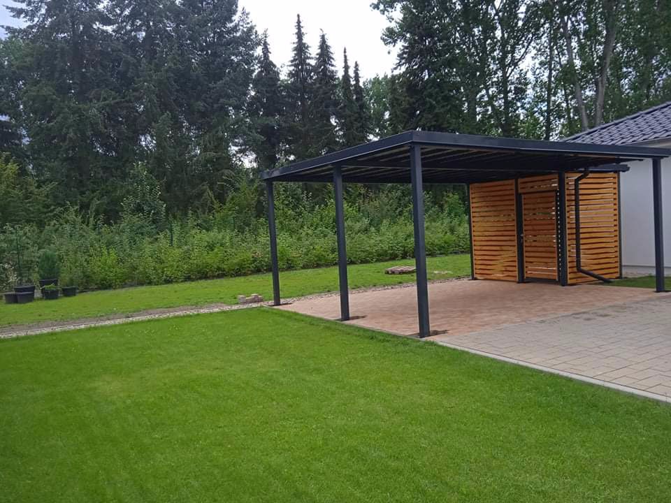 Nowoczesna wiata garażowa z czarną metalową konstrukcją i drewnianym panelem bocznym, widok z trawnika.