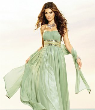 Kobieta w długiej, zwiewnej, miętowej sukni bez ramiączek z ozdobnym, złotym pasem, prezentująca kreację z rozwianymi włosami i delikatną biżuterią.