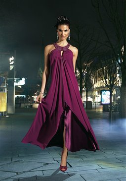 Modelka w długiej, fioletowej sukni wieczorowej z rozcięciem, ozdobny dekolt, na tle nocnej scenerii miejskiej.