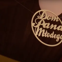 Drewniany, okrągły napis 'Dom Pana Młodego' zawieszony na żyłce, z fragmentem różowego balonu w tle, na tle drewnianego sufitu.