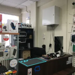 Wnętrze punktu sprzedaży akcesori&oacute;w do telefon&oacute;w: regały z uchwytami samochodowymi, ładowarkami bezprzewodowymi i etui, lada z terminalem płatniczym i naklejkami Google i Facebook, kamera...