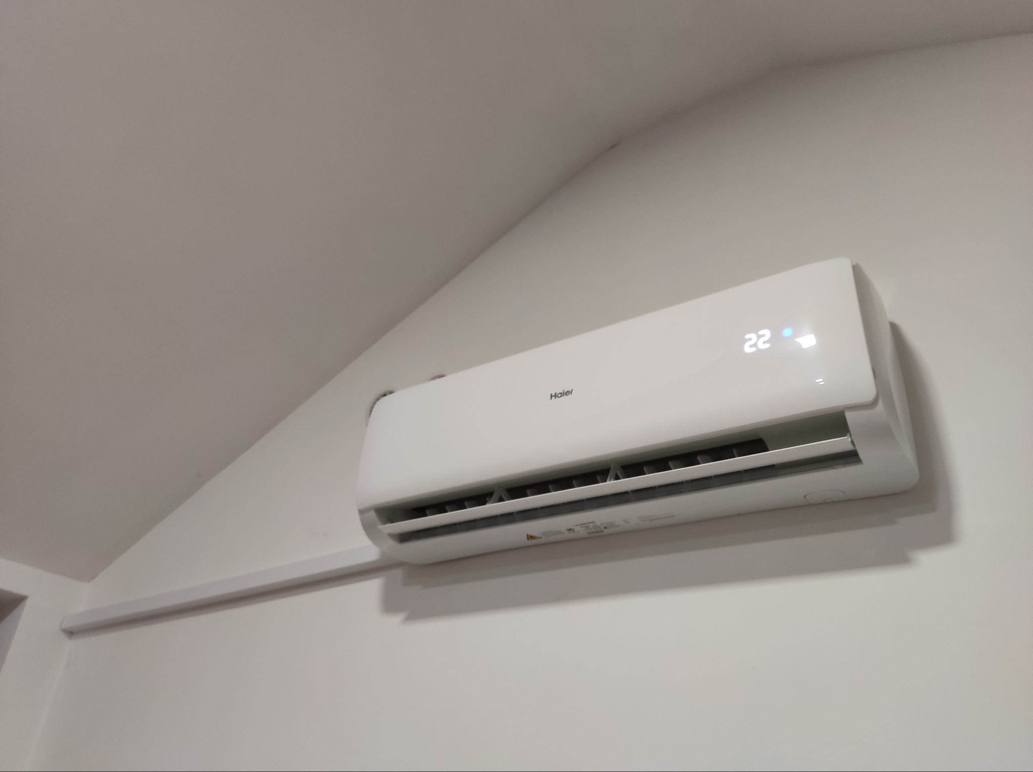 Biały klimatyzator Haier z wyświetlaczem ustawionym na 22 stopnie Celsjusza, zamontowany na ścianie w Opocznie, z widoczną listwą przypodłogową.