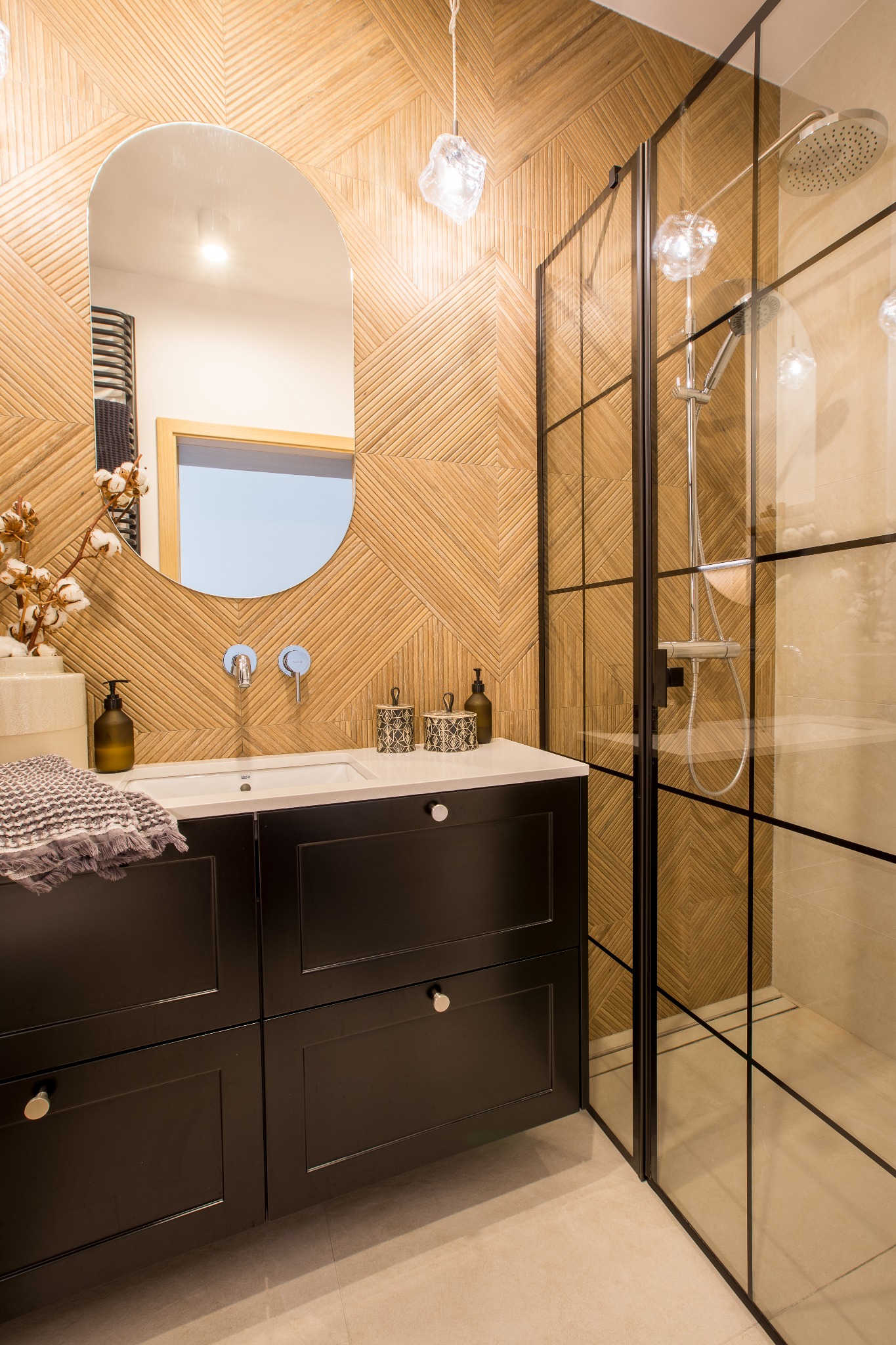 Nowoczesna łazienka z kabiną prysznicową w stylu loft, drewnianą mozaiką na ścianie, owalnym lustrem i czarną szafką pod umywalką.