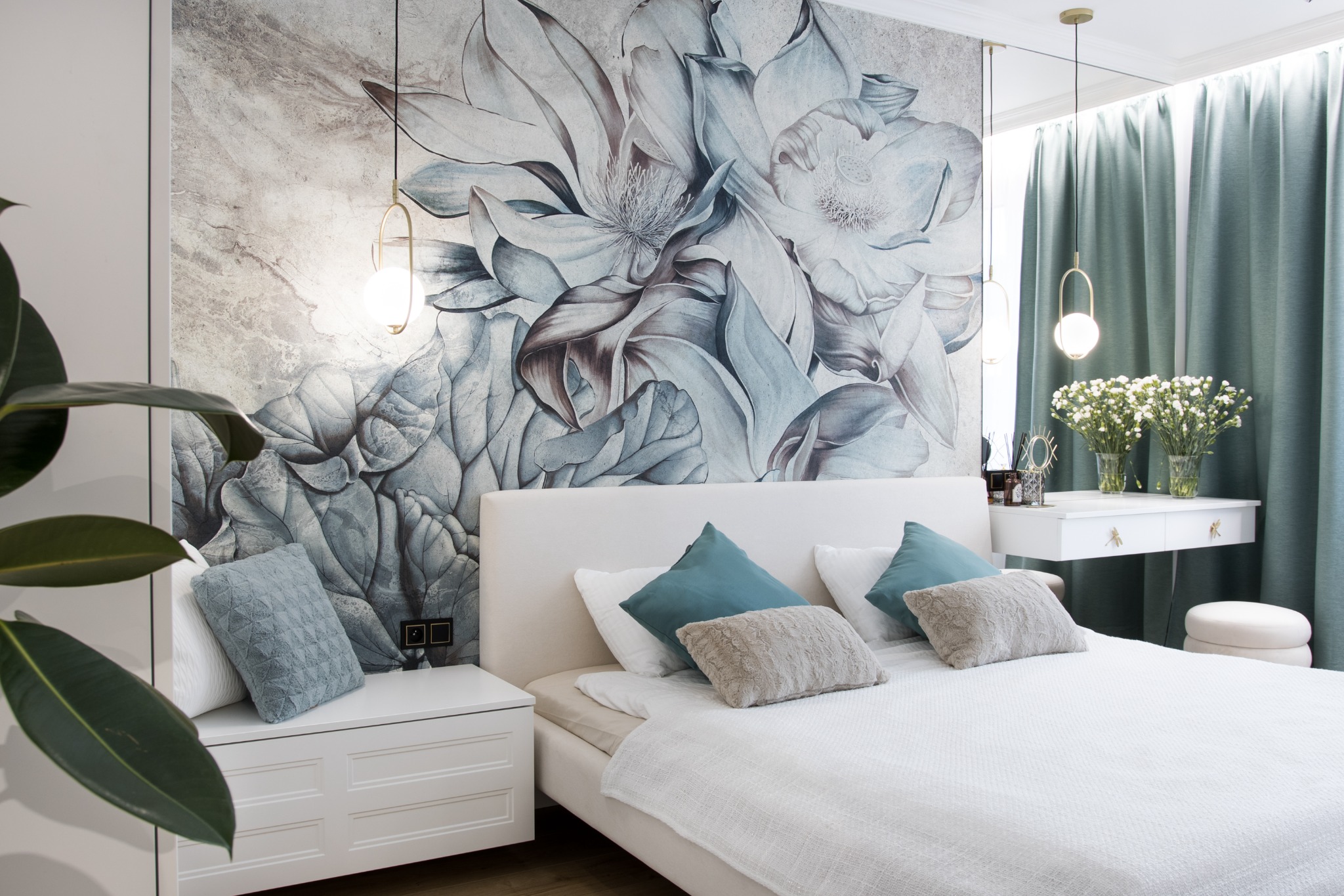 Elegancka sypialnia z łóżkiem w odcieniach bieli i szarości, akcentem kolorystycznym w postaci turkusowych poduszek i dekoracyjną tapetą z motywem kwiatowym oraz wiszącymi lampami.